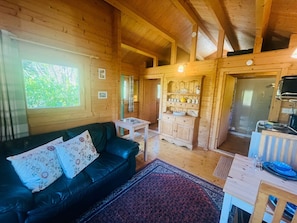 Interior de una cabaña de madera con sofá, una mesita, un armario y un comedor.
