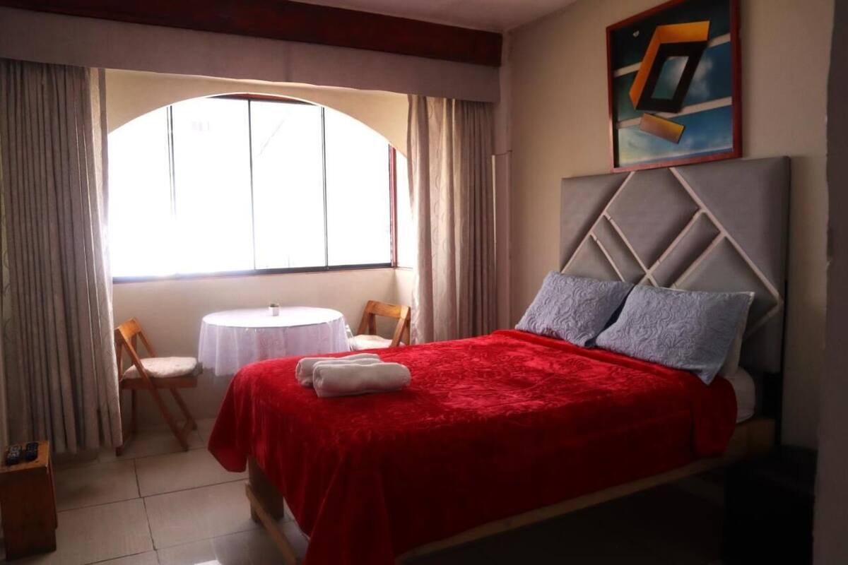 Una camera d'albergo con un letto, un piccolo tavolino rotondo, due sedie e una finestra con tende.