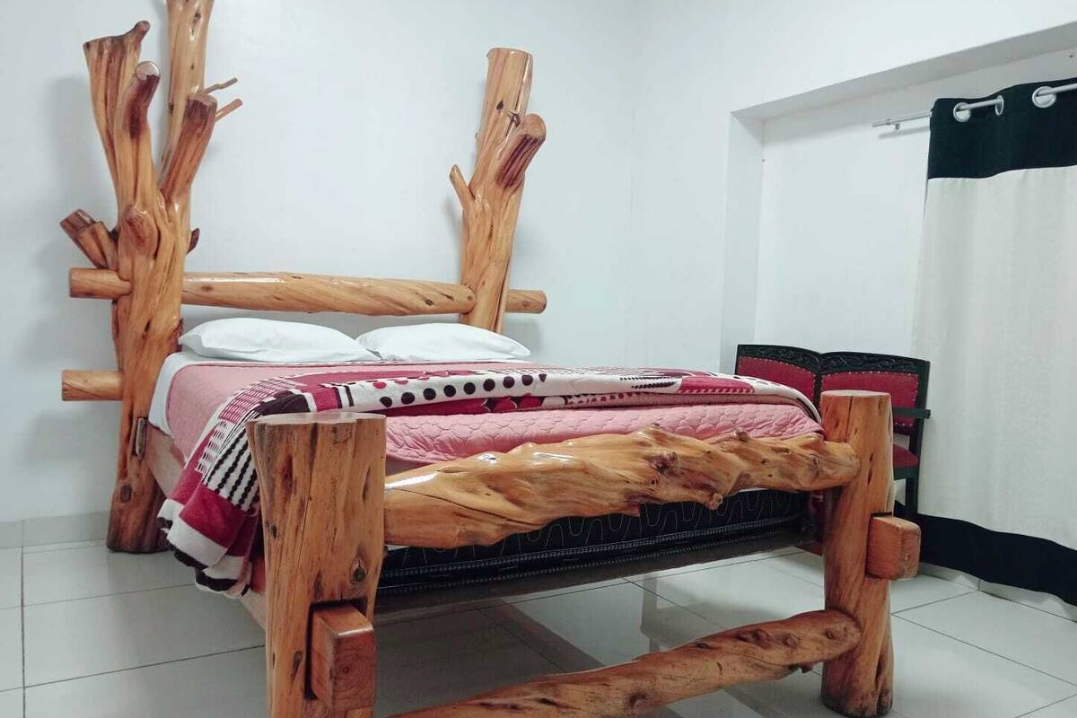Un letto con una struttura in legno particolare, una parete bianca e una sedia rossa.