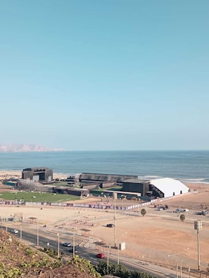 A coastal sports complex with a stadium, parking areas, and a road leading to the beach. - Costa 21 (Lima)