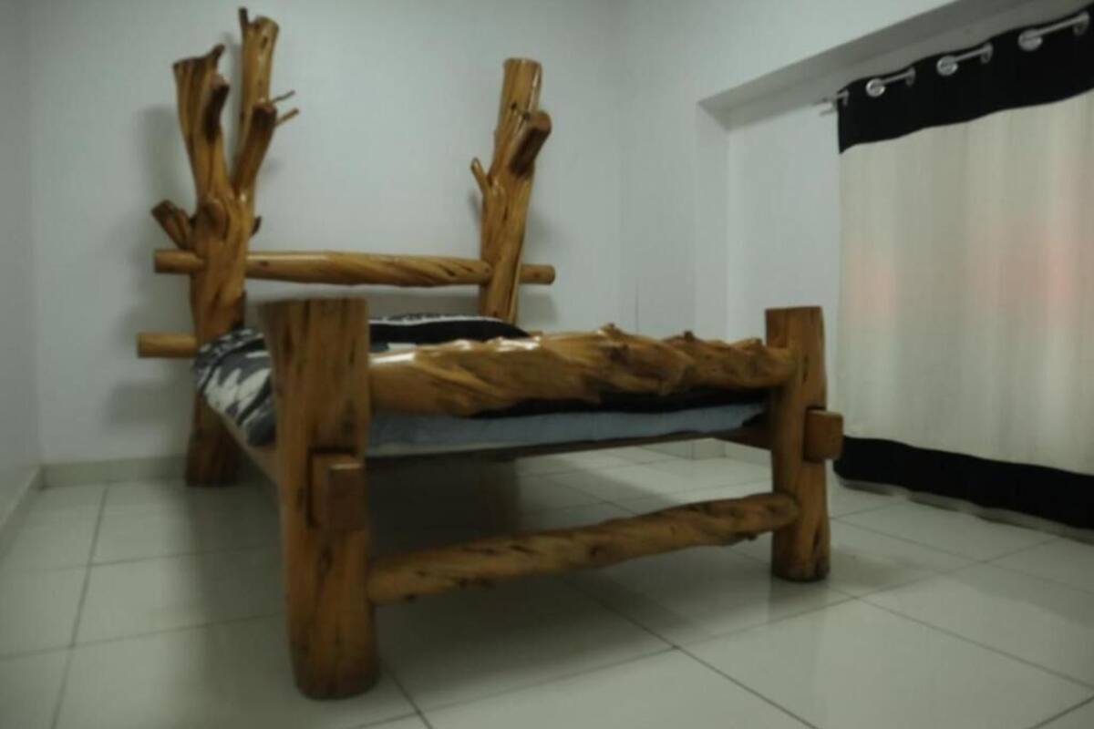 Una panca in legno dal design originale, collocata in una stanza con pareti bianche e pavimento piastrellato.