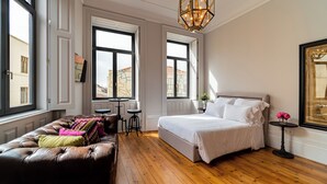 A bedroom with a large bed, a leather sofa, a small table, and a chandelier. - 18th Century Italia Suite w/ Historic Charm & Modern Luxury in Central Porto 2N (Porto)