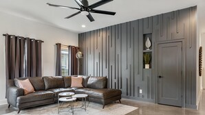 Una sala moderna con un sofá modular, un ventilador de techo y un panel decorativo en la pared.