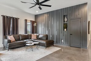A modern living room with a sectional sofa, a ceiling fan, and a decorative wall panel.