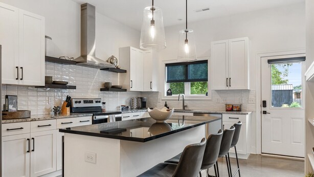 Una cocina moderna con armarios blancos, encimera negra y una isla central con taburetes de bar.