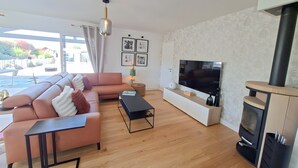 A modern living room with a sectional sofa, a flat-screen TV, a fireplace, and a view of the outdoors. - 5-Room Villa with Pool and Terrace in Le Porge (Le Porge)
