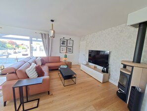 A modern living room with a sectional sofa, a flat-screen TV, a fireplace, and a view of the outdoors. - 5-Room Villa with Pool and Terrace in Le Porge (Le Porge)
