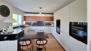A modern kitchen with white cabinets, a black countertop, and a dining area with a table and chairs. - 5-Room Villa with Pool and Terrace in Le Porge (Le Porge)