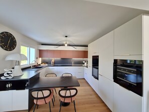 A modern kitchen with white cabinets, a black countertop, and a dining area with a table and chairs. - 5-Room Villa with Pool and Terrace in Le Porge (Le Porge)