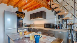 A modern kitchen with a wooden ceiling, stainless steel appliances, and a stone wall.