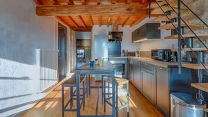 A modern kitchen with wooden beams, a dining area with stools, and a staircase.