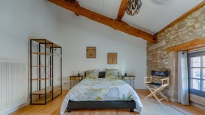 A bedroom with a bed, a wooden wardrobe, a director's chair, and stone walls.