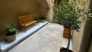 A narrow corridor with a bench, potted plants, and a wall-mounted air conditioning unit.