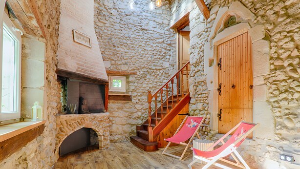 A stone-walled room with a fireplace, wooden staircase, and two beach chairs.