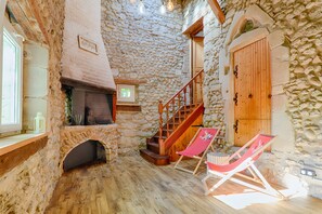 Ein Zimmer mit Steinwänden, einem Kamin, einer Holztreppe und zwei Strandstühlen.