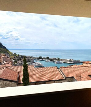 A coastal town with terracotta-roofed buildings, a marina with boats, and a clear view of the sea. - Levante - Portopiccolo Apartments (Sistiana)