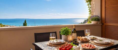 Mesa dispuesta para una comida con vistas al mar, una botella de vino y diversos alimentos.