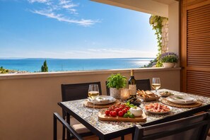 Ein Tisch, gedeckt für eine Mahlzeit, mit Blick auf das Meer, einer Weinflasche und verschiedenen Speisen.