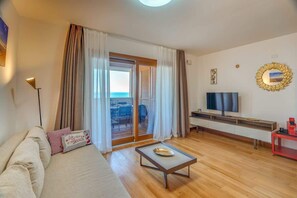 Un soggiorno moderno con un divano, un tavolino, una TV e una porta vetrata scorrevole che dà su uno spazio esterno.