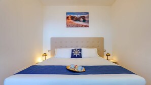 Una cama bien hecha con un edredón azul, una almohada decorativa y una bandeja con tazas y una tetera.
