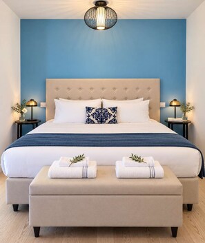 A hotel room with a large bed, a headboard, two bedside tables with lamps, a blue wall, and a wooden floor. - Sole Mio - Portopiccolo Apartments (Duino Aurisina)