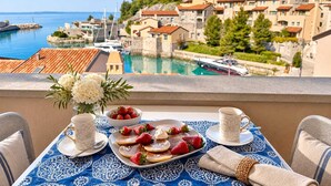 Un balcon avec une table préparée pour le petit-déjeuner, offrant une vue sur une ville côtière, avec ses bâtiments historiques et son port de plaisance.