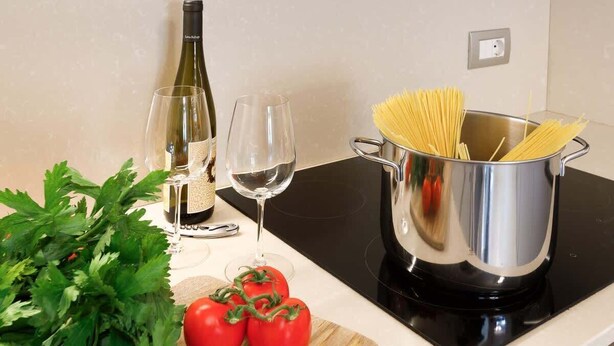 Un plan de travail de cuisine avec un pot de spaghettis crus, deux verres à vin, une bouteille de vin, ainsi que des tomates et du persil frais.
