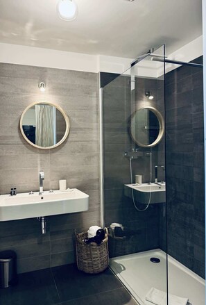 Un bagno moderno con cabina doccia in vetro, uno specchio rotondo, un lavandino con rubinetto e un cesto in vimini.