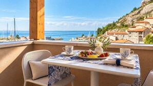 Un balcon avec une table dressée pour deux personnes, offrant une vue sur la côte, avec des bâtiments et la mer en toile de fond.