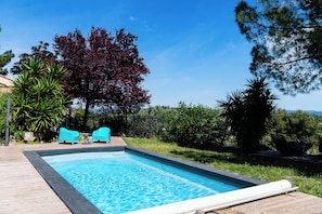 Ein rechteckiger Pool mit einer Holzterrasse, zwei türkisfarbenen St ühlen und einem Baum mit roten Blättern.
