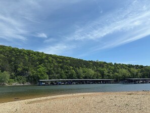 A lakeside view with a dock and covered structures, surrounded by dense forest.
