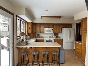 A kitchen with wooden cabinets, a microwave, stove, refrigerator, and three bar stools.