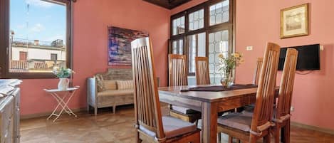 Un comedor con mesa y sillas de madera, un sofá, una ventana con vistas y un cuadro en la pared.