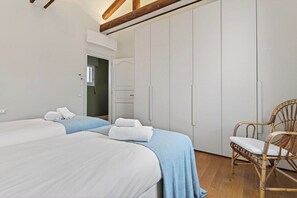 A bedroom with two beds, a wardrobe, a chair, and a door leading to another room. - Dimora San Leonardo (Venezia)