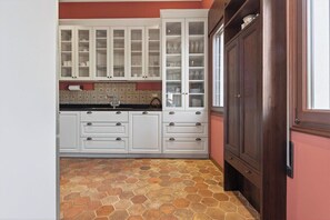 A kitchen with white cabinets, a tiled backsplash, and a stone-patterned floor. - Dimora San Leonardo (Venezia)