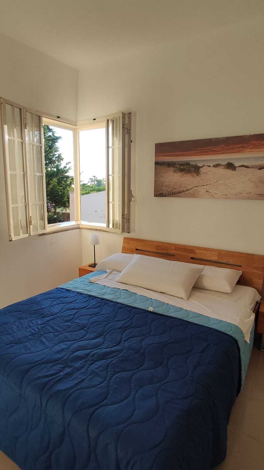 A bedroom with a bed, a nightstand, a window with curtains, and a painting on the wall.