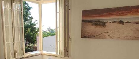A bedroom with a bed, a nightstand, a window with curtains, and a painting on the wall.