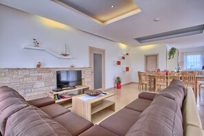 Ein modernes Wohnzimmer mit Steinwand, einem Flachbildfernseher, einem Essbereich mit Holzmöbeln und einer Küche im Hintergrund.