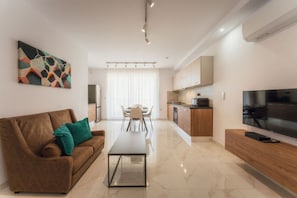 A modern living room with a sofa, coffee table, and TV. There is a kitchen area with cabinets and a dining table. - Modern Apt in St. Paul's Bay with sea view (St Pauls Bay)