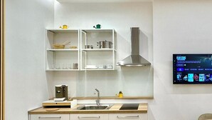 Uma cozinha moderna com armários brancos, coifa de aço inoxidável, TV integrada e piso com padrão em herringbone.