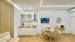 Uma cozinha moderna com prateleiras embutidas, uma área de jantar com mesa redonda e cadeiras, e uma TV fixada na parede.