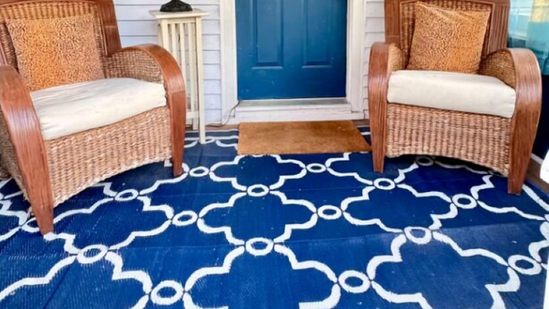Eine Veranda mit zwei Korbstühlen, einer blauen Tür und einem gemusterten Teppich.