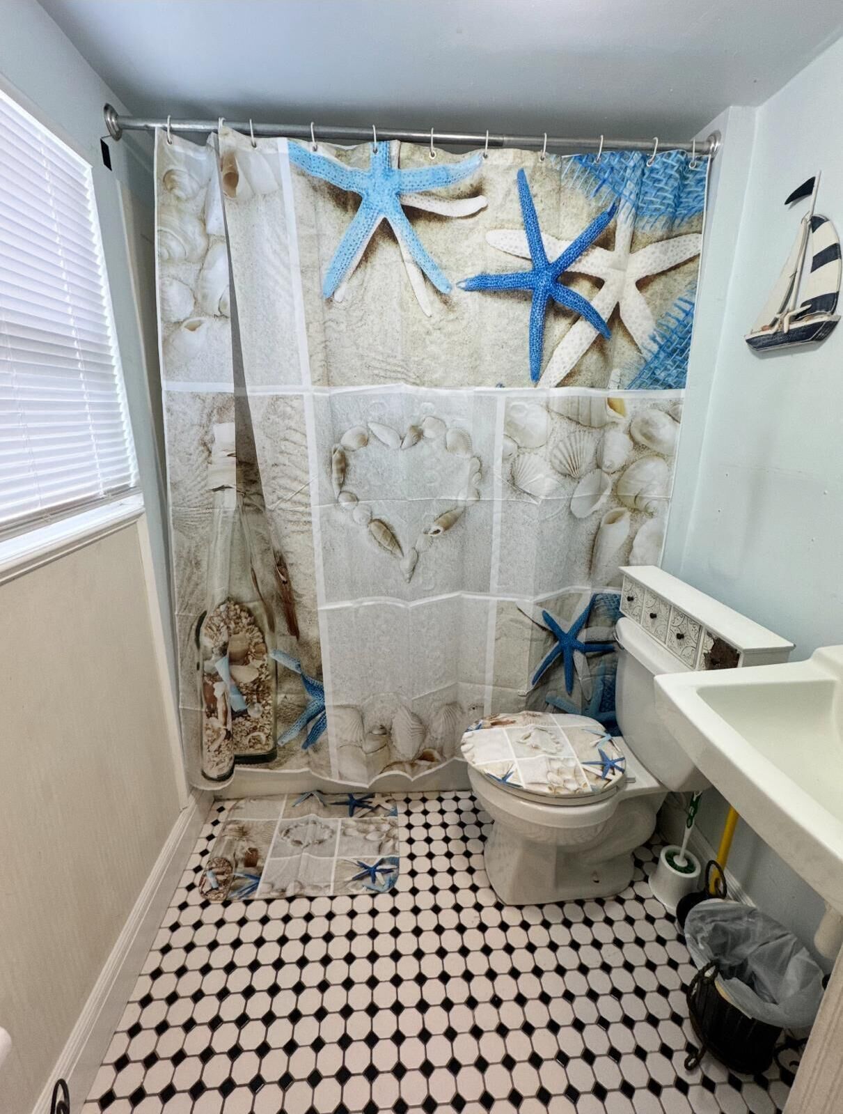 A bathroom with a black and white checkered floor, a shower curtain with starfish and seashells, and a toilet with a decorative cover.