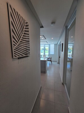 A modern hallway with a leaf-patterned wall art, a dining area with a table and chairs, and a view of the outdoors through large windows. - New Remodeled 1BR· 2 Queen Beds+Full Kitchen+ Pool (Isabela)