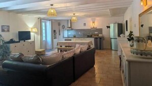 Amplia sala de estar con un sofá, televisión y cocina al fondo.