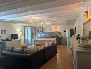 A spacious living area with a sofa, a television, and a kitchen in the background.