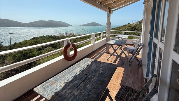 Un espacio al aire libre techado con vista al mar, bancos de madera y un columpio de cuerda.