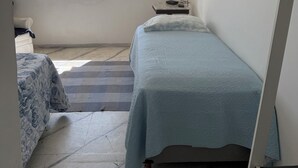 Un dormitorio con cama, televisor, ventana que ofrece vistas a la costa y ventilador de techo.