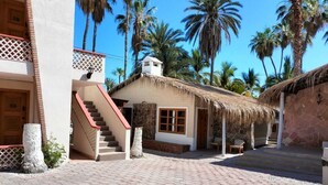 A building with a staircase, a thatched-roof structure, and palm trees.
