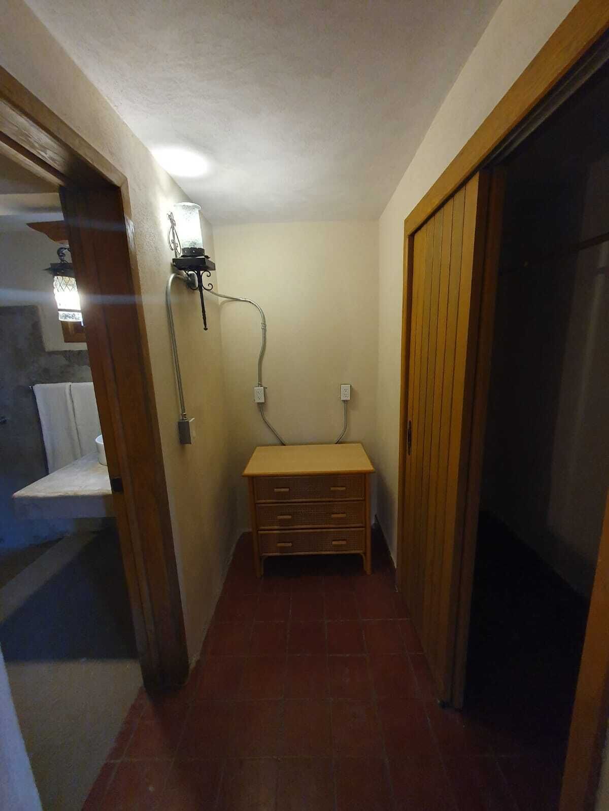 Un couloir étroit avec un banc en bois, une prise électrique fixée au mur et une porte sur la droite.